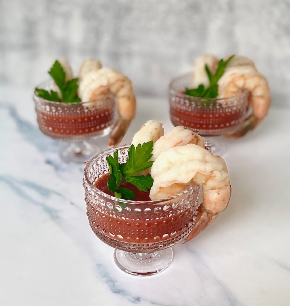 3 clear glasses with jumbo shrimp, sauce and parsley