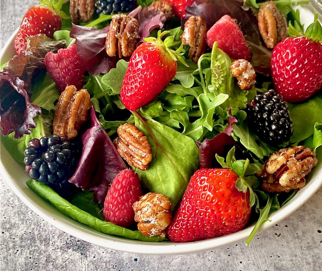a bowl of strawberries, raspberries, blackberries and mixed greens