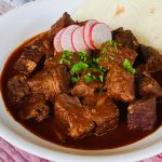 Chile Colorado with cilantro and radishes in a white bowl