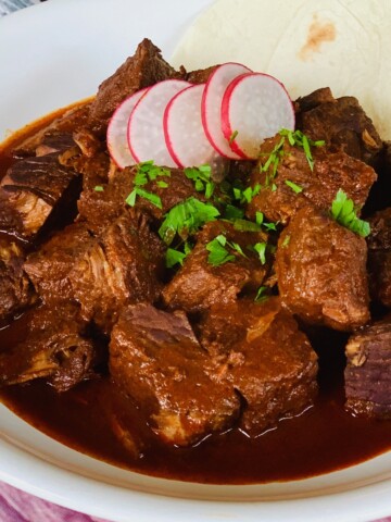Chili Colorado in white bowl with radish slices