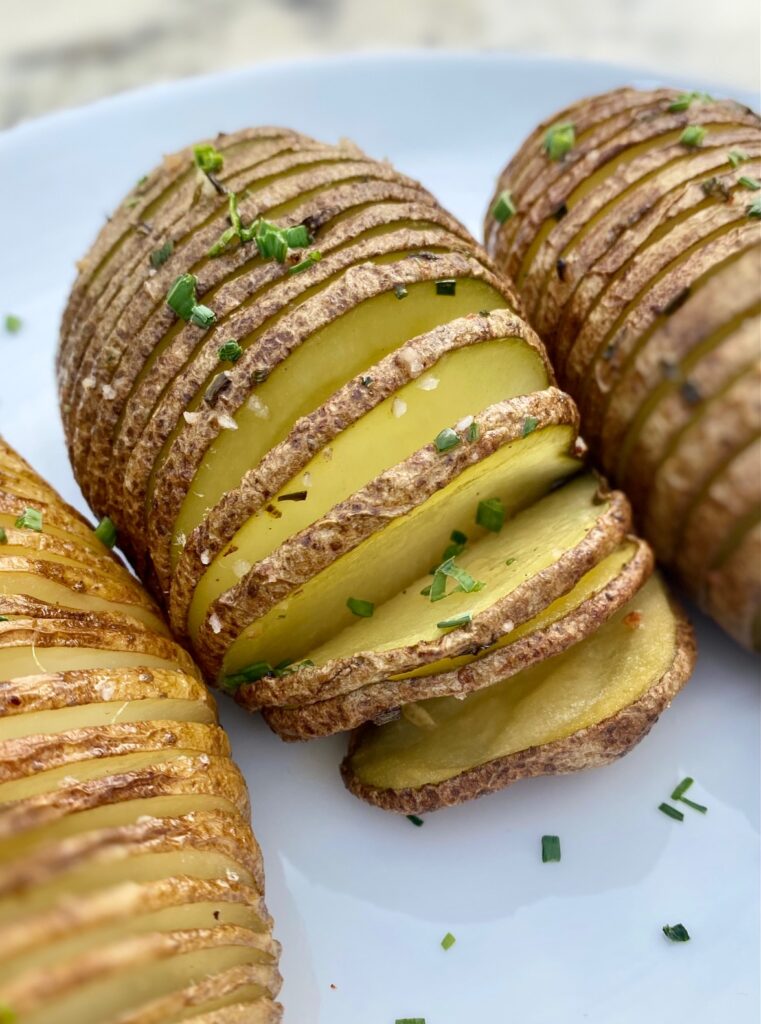 3 sliced hasselback style potatoes on white plate
