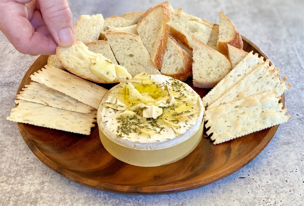 a hand dipping bread into brie