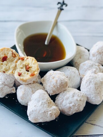 Black plate of Beignets with white bowl of maple syrup