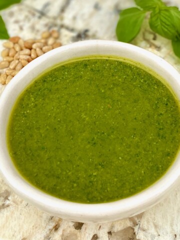 white bowl of pesto with pine nuts and basil