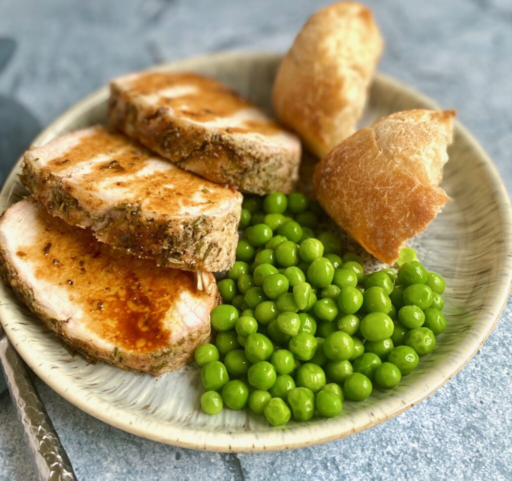 a plate of pork roast, bread and peas