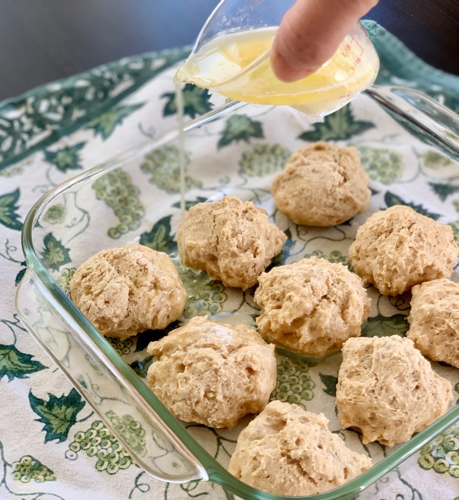 Pouring butter over beer bread rolls in a glass pan