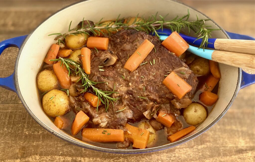 spoons in pan of roast with potatoes and carrots