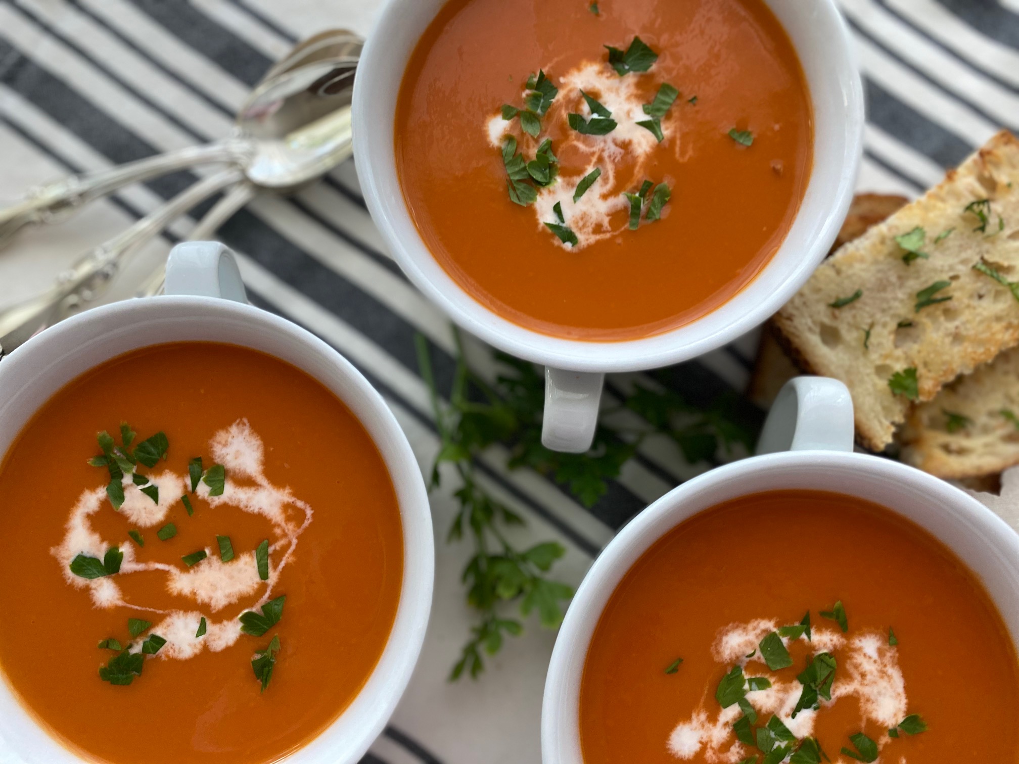 3 bowls Roasted Tomato Soup with spoons and garlic bread
