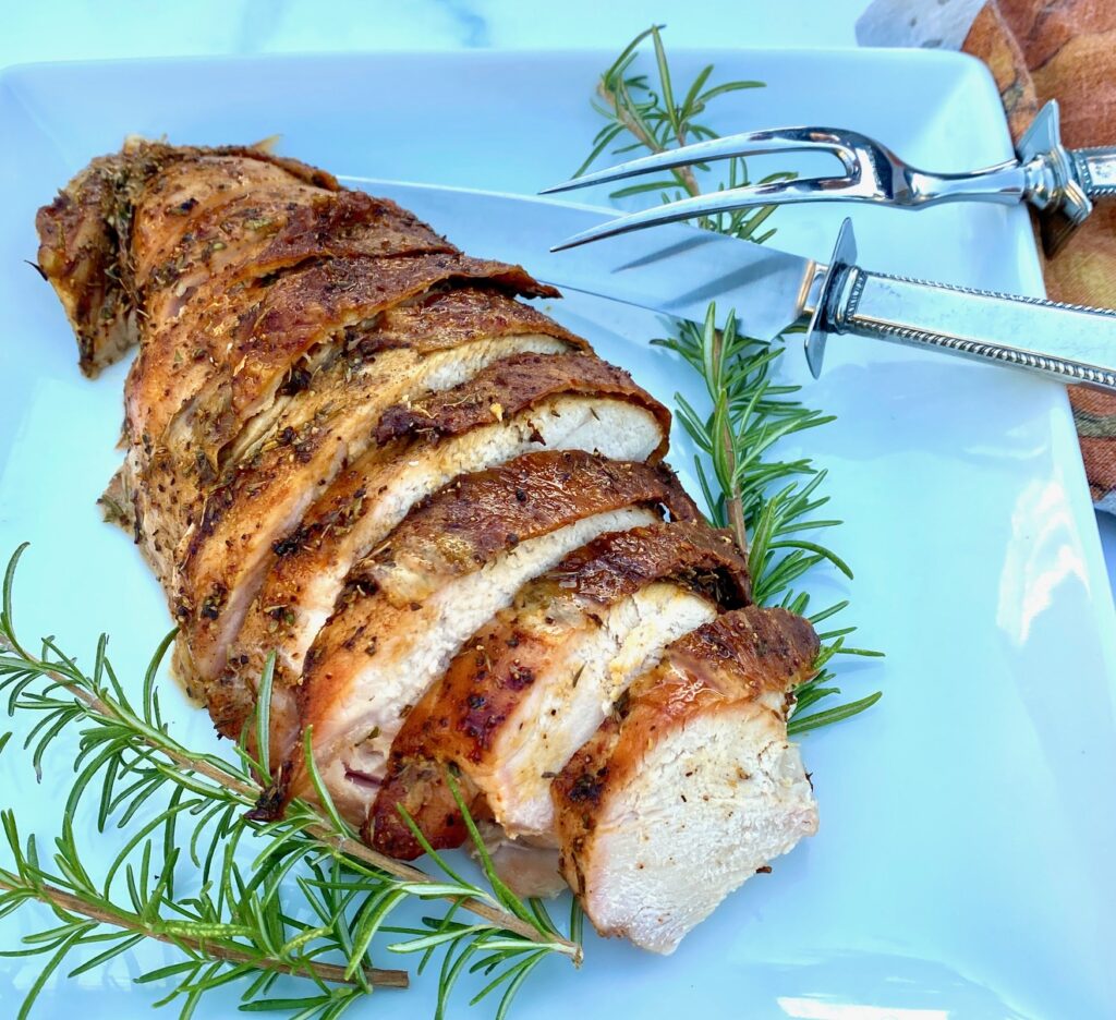 a white platter of roasted turkey with a carving knife and fork