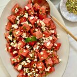 white platter with watermelon salad, spoon and nuts