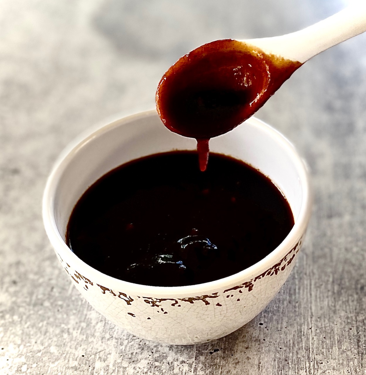white spoon dripping sauce into bowl