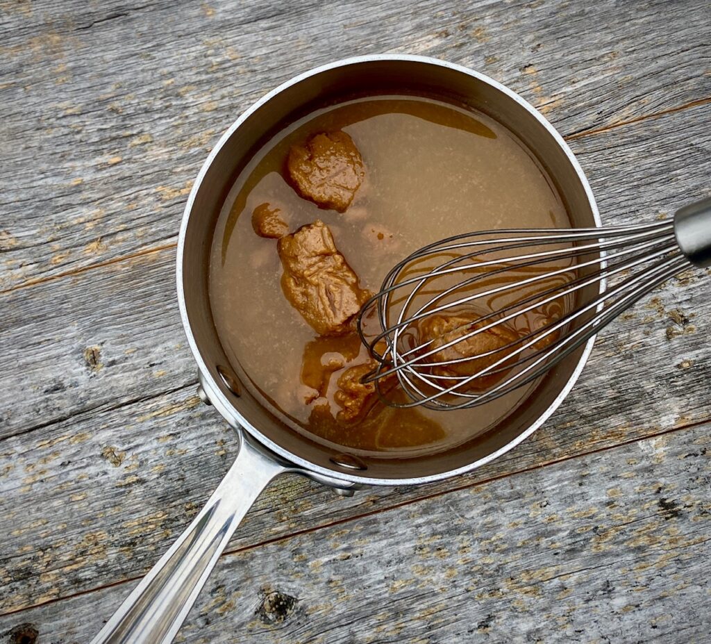 Yellow miso in pan with sauce and whisk